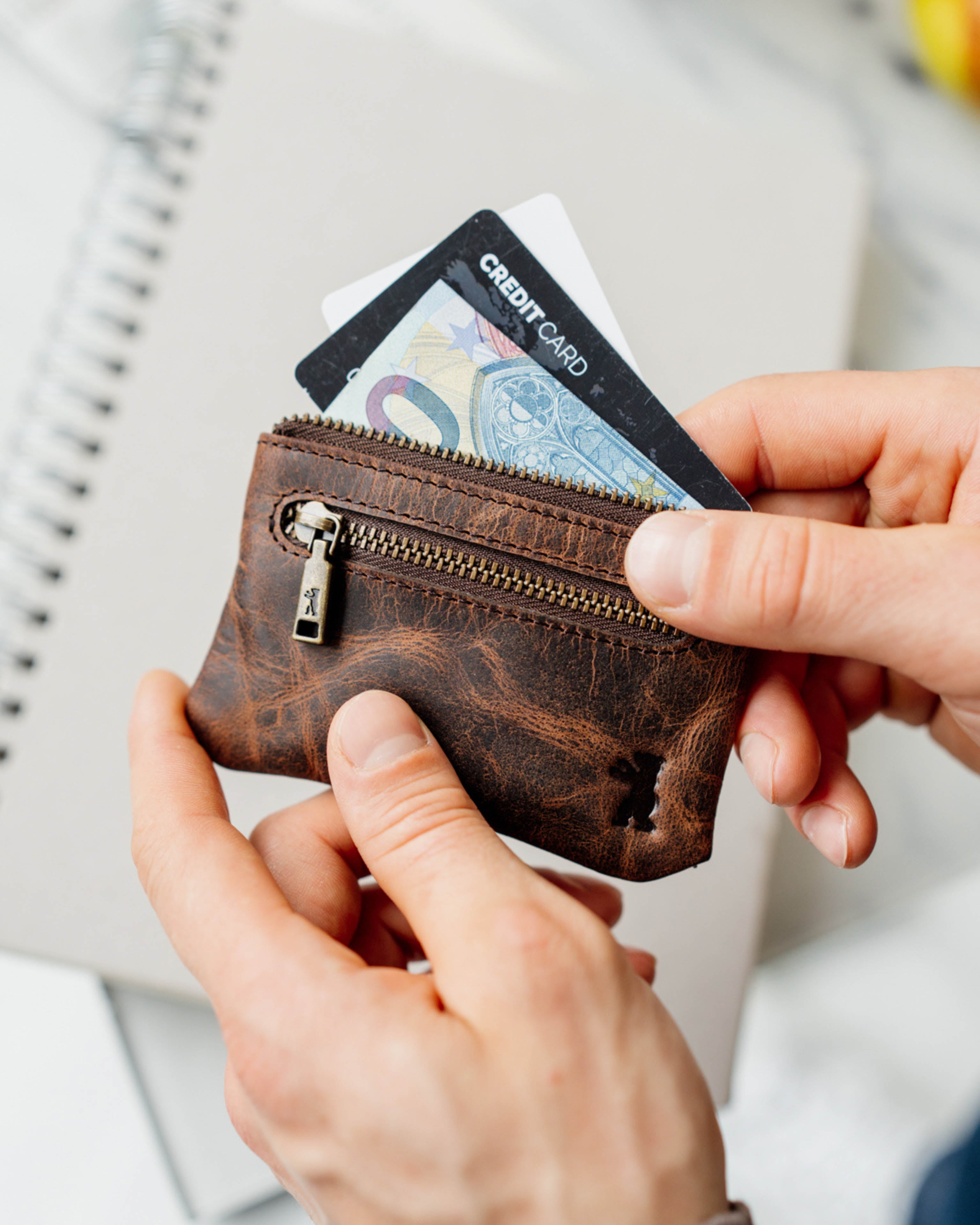 Person holding a earth leather key pouch with a credit card inside