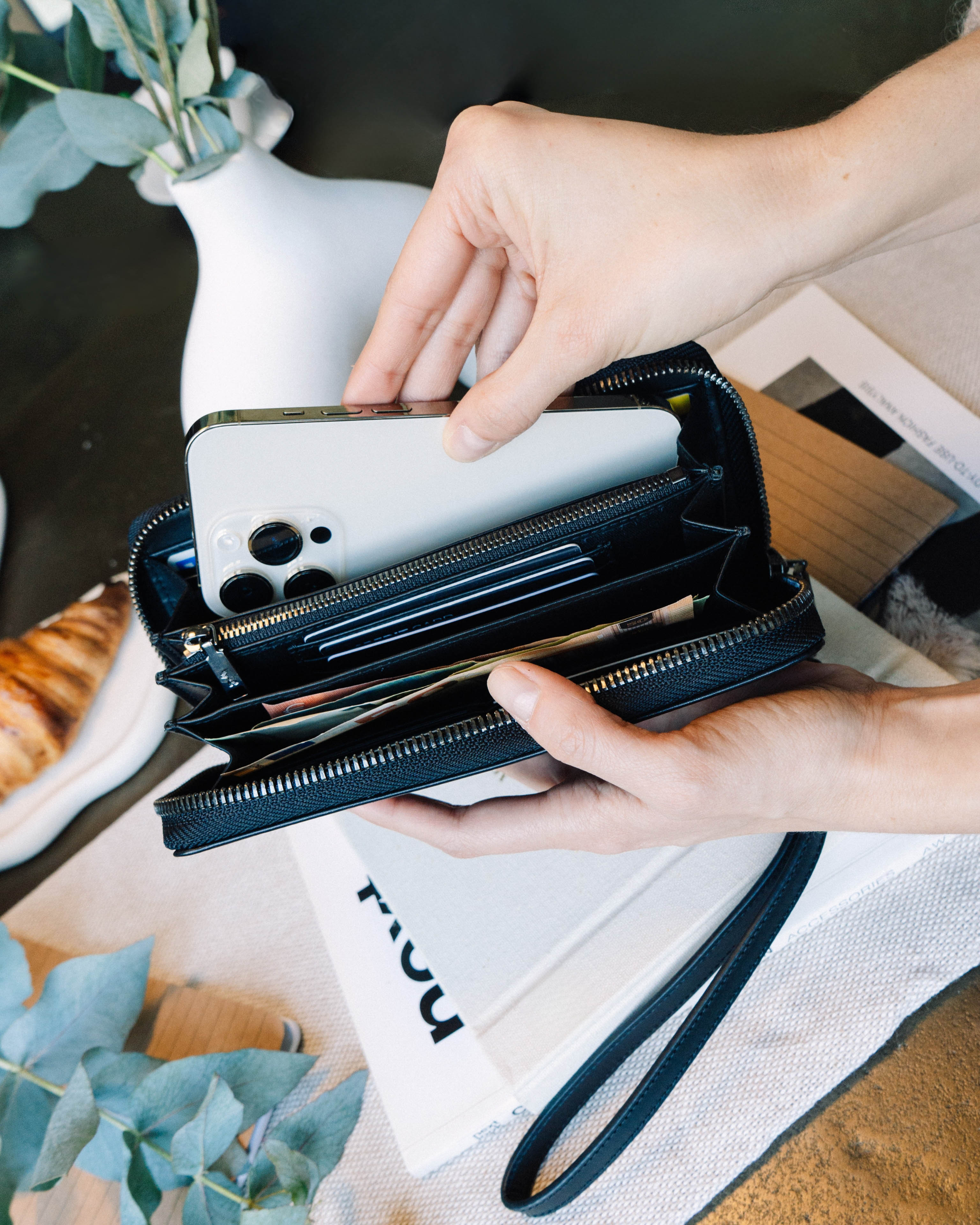 Hands placing a smartphone into an open black emboss leather wallet.