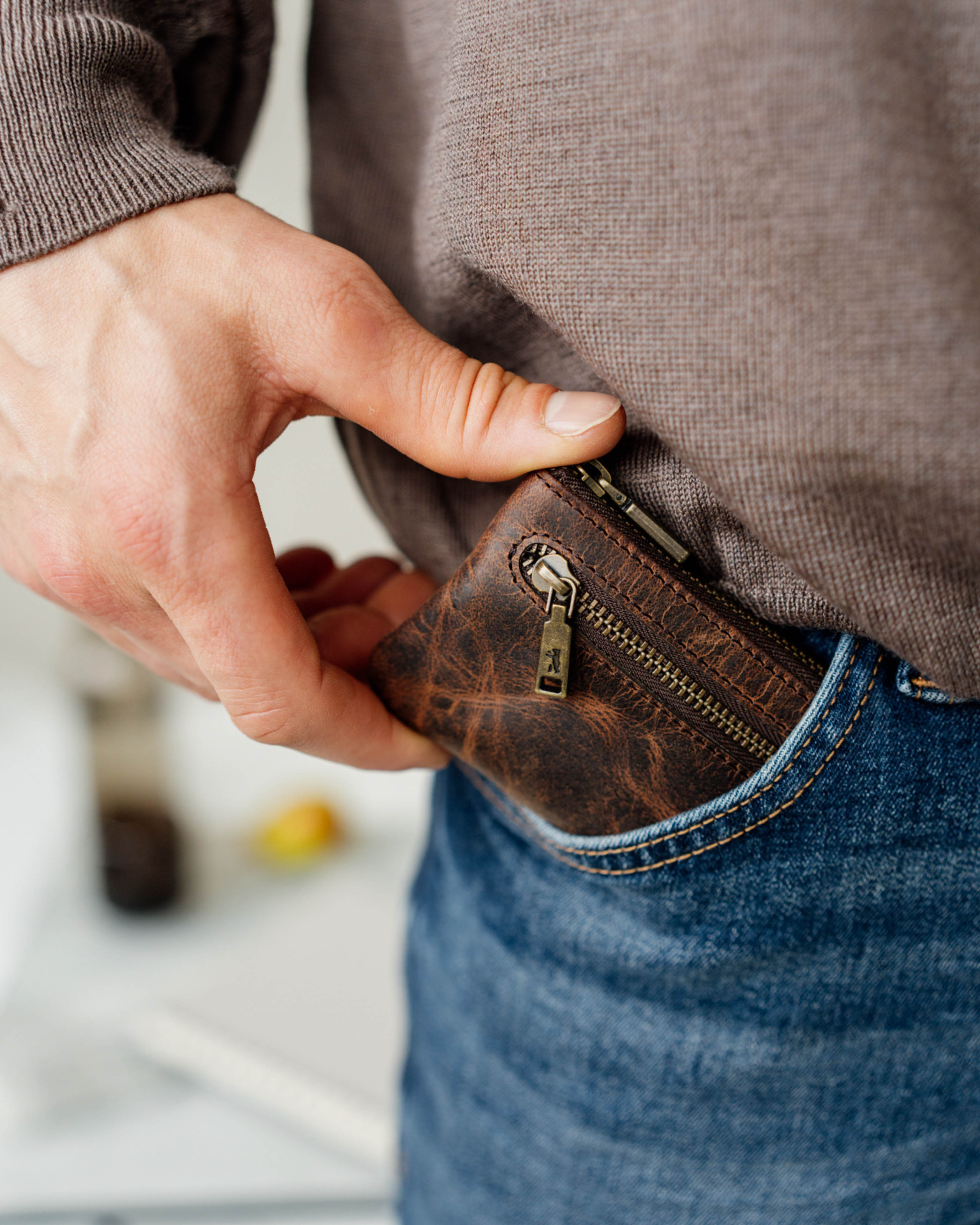Hand placing a small earth leather key pouch into a jeans pocket.