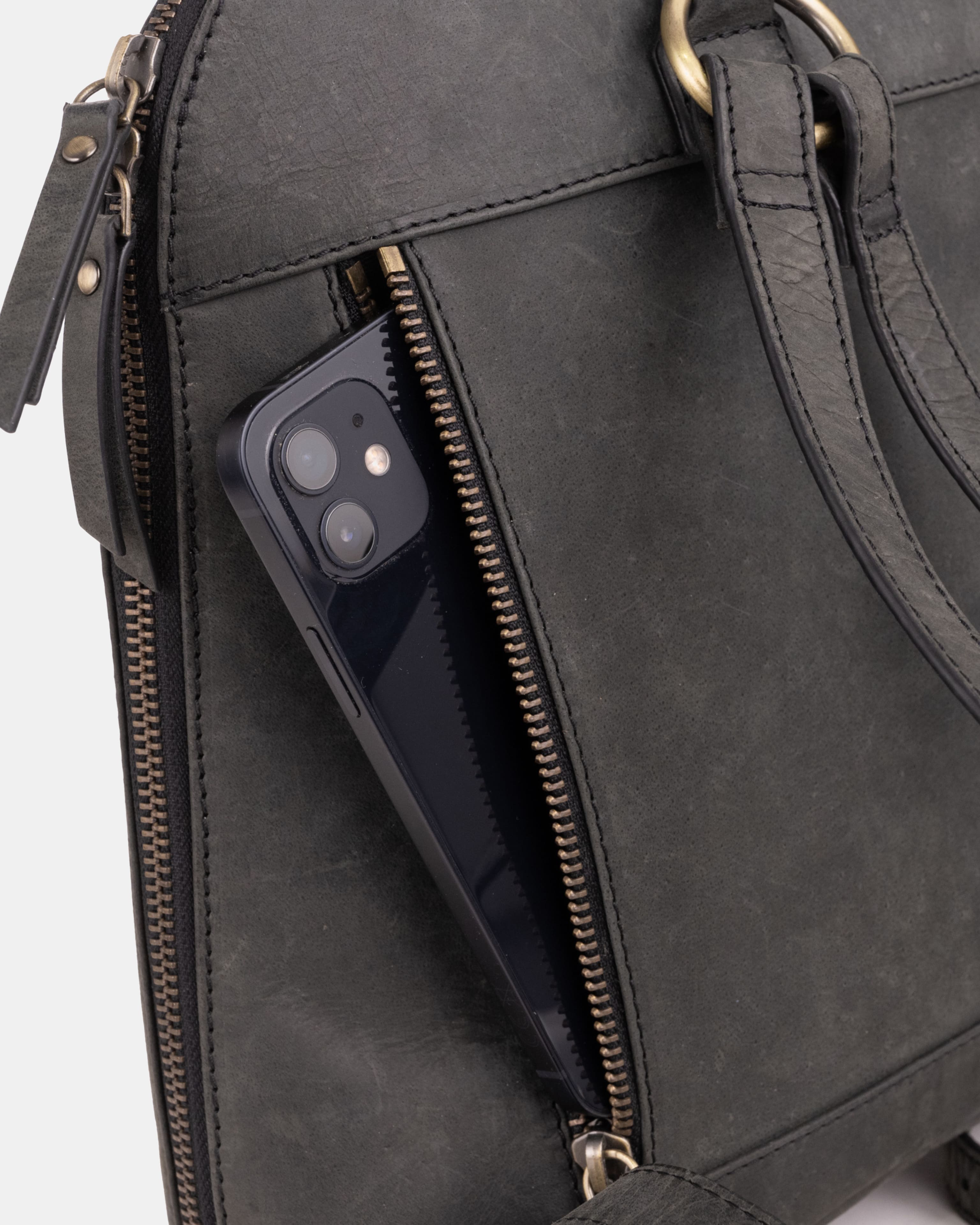 Close-up smartphone sliding into a dark grey leather backpack zipper pocket.