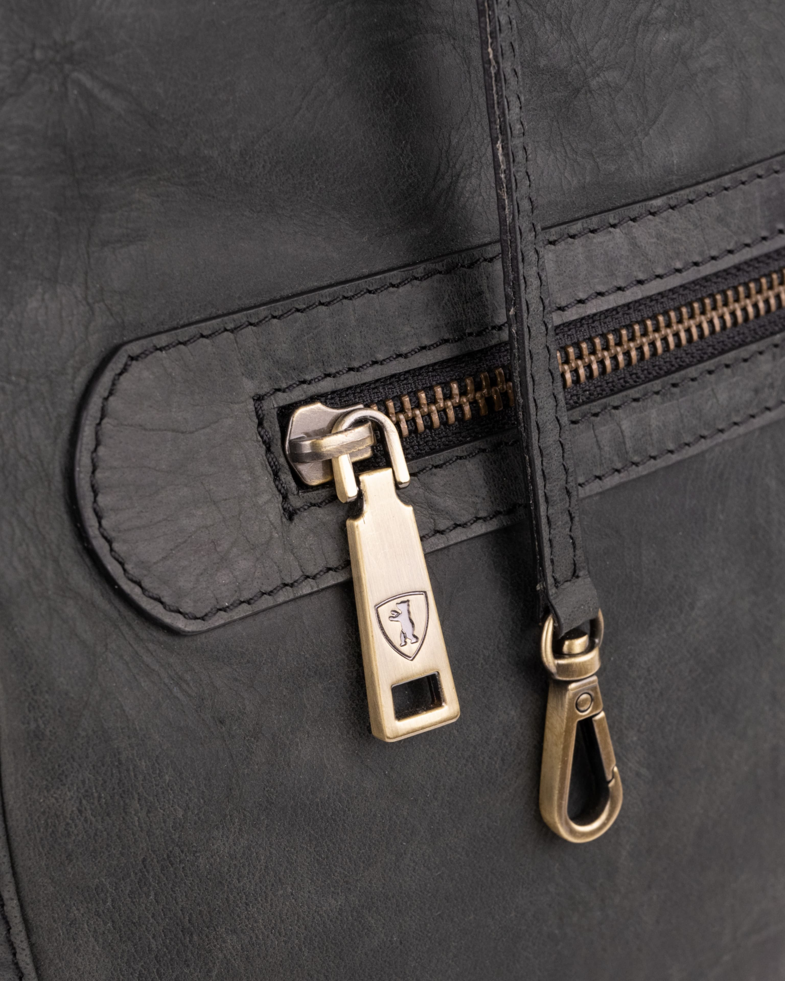 Close-up of dark grey leather backpack zipper with metallic branding.