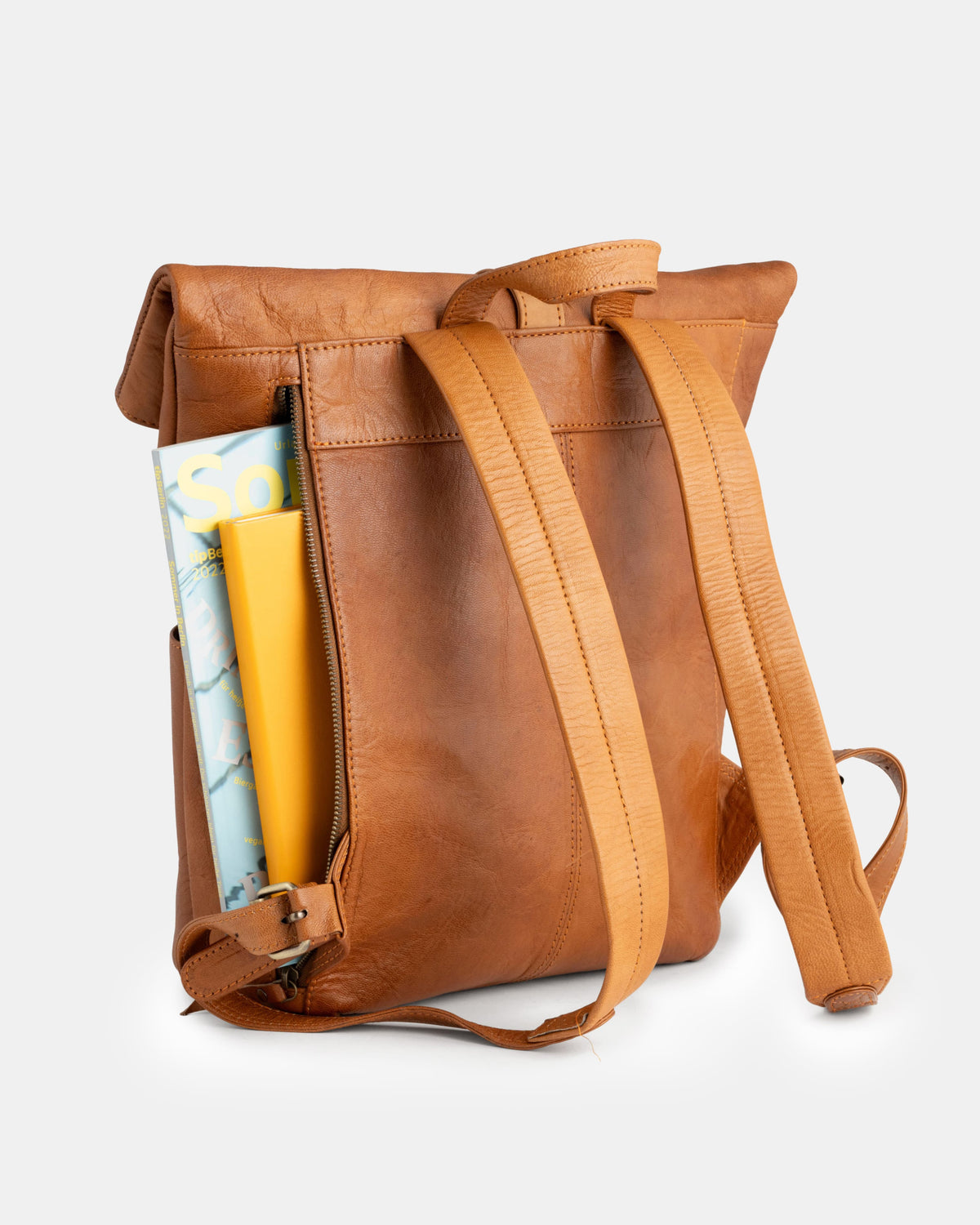 View of magazines sliding into the zippered side pocket of a vintage backpack.