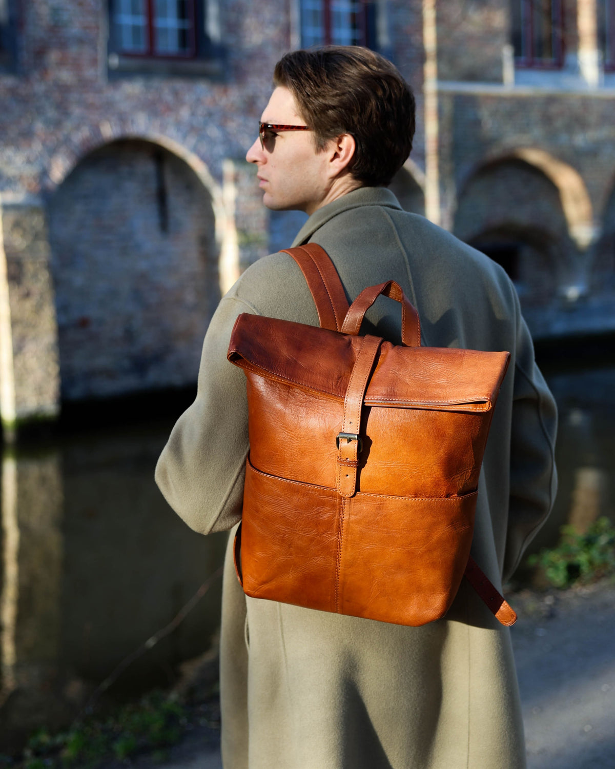 Shot of man wearing vintage leather roll-top backpack against scenic backdrop.