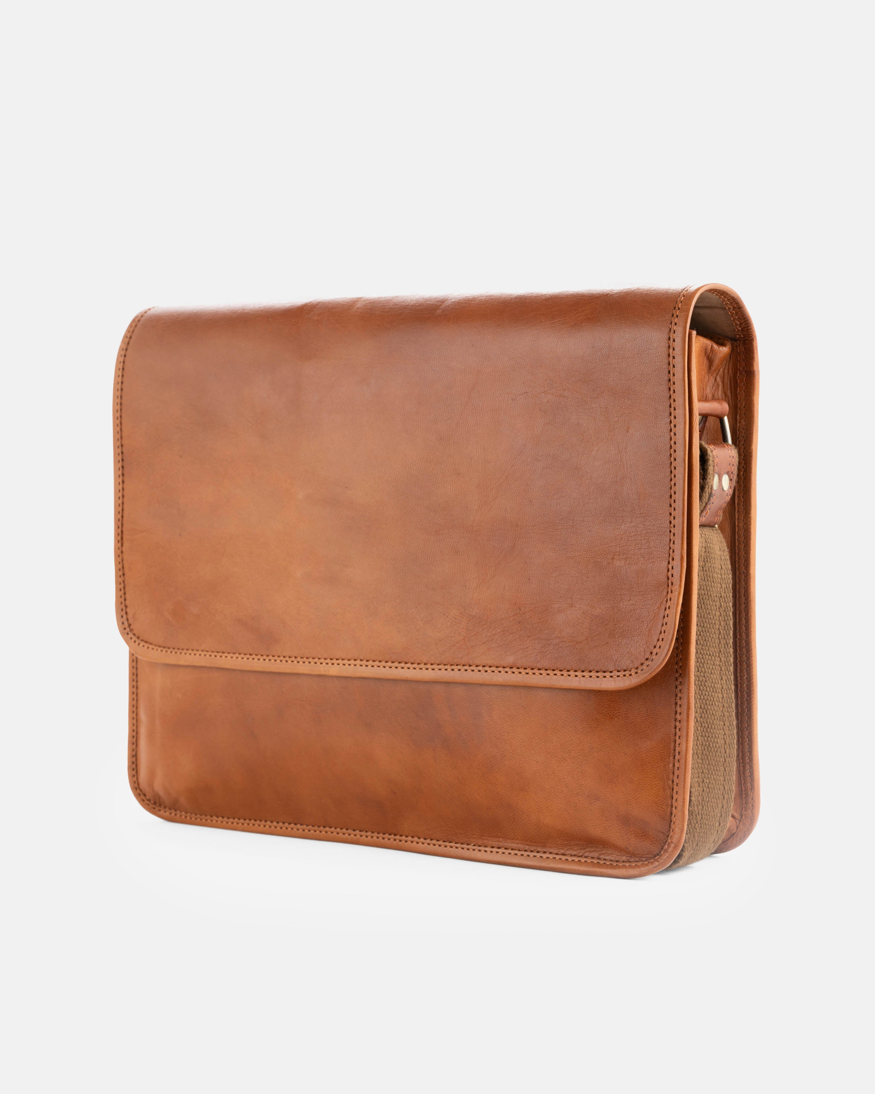 Angled front-left view of a minimalist vintage leather messenger bag featuring a clean, unadorned closing flap and a fabric-lined leather shoulder strap attached to the side