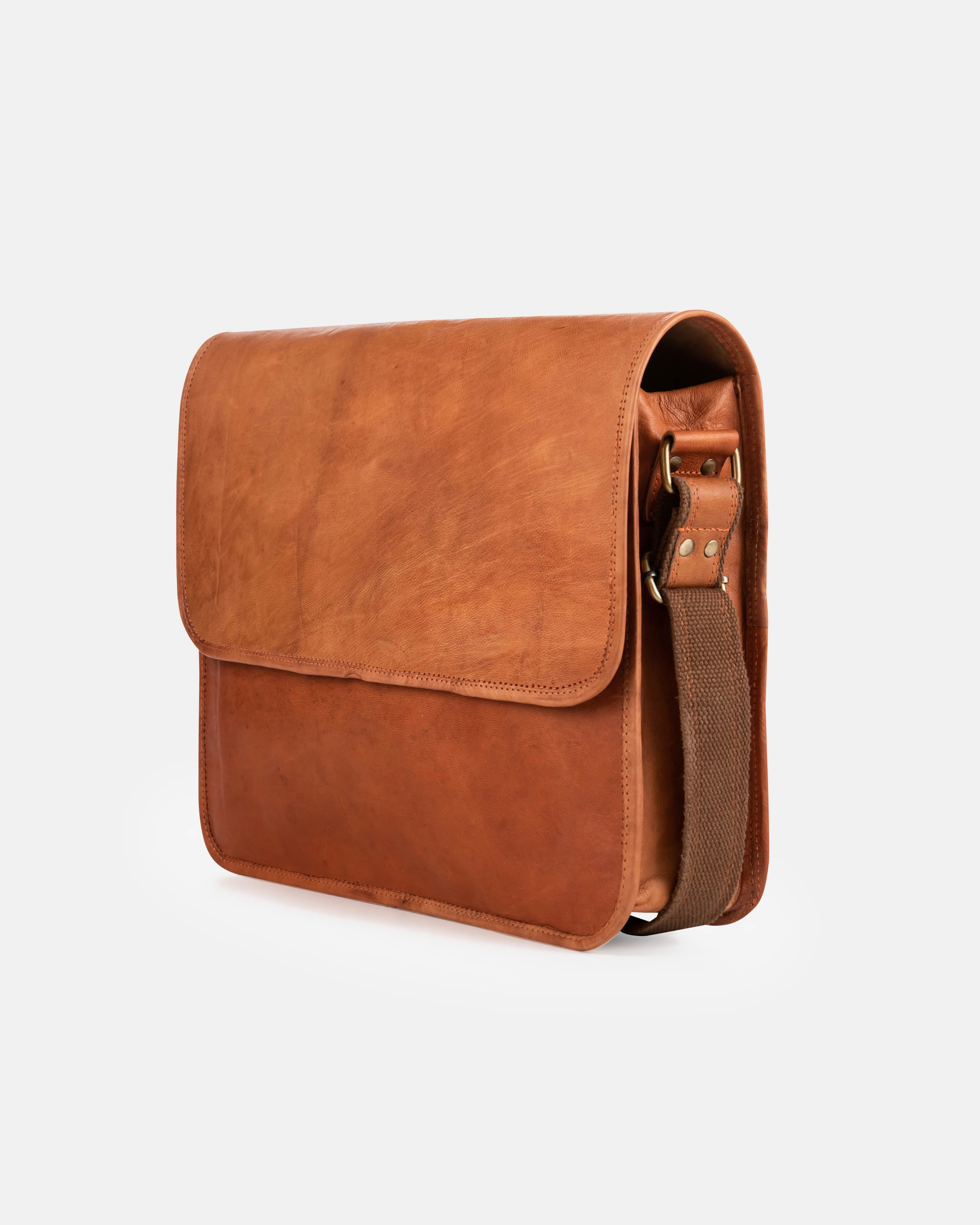 Angled front-right view of a minimalist vintage leather messenger bag featuring a clean, unadorned closing flap and a fabric-lined leather shoulder strap attached to the side