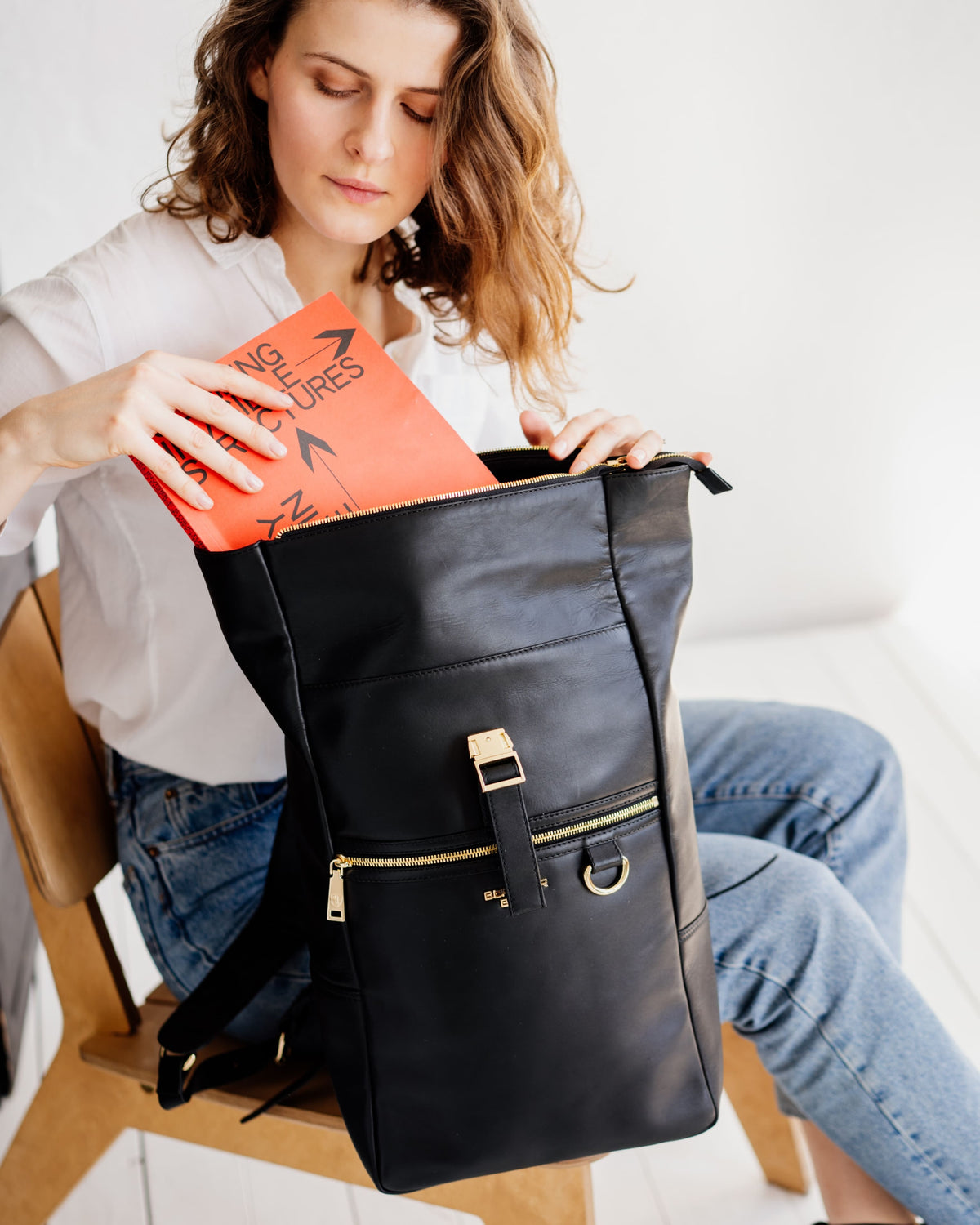 Woman sliding a book into an open black leather backpack with gold hardware