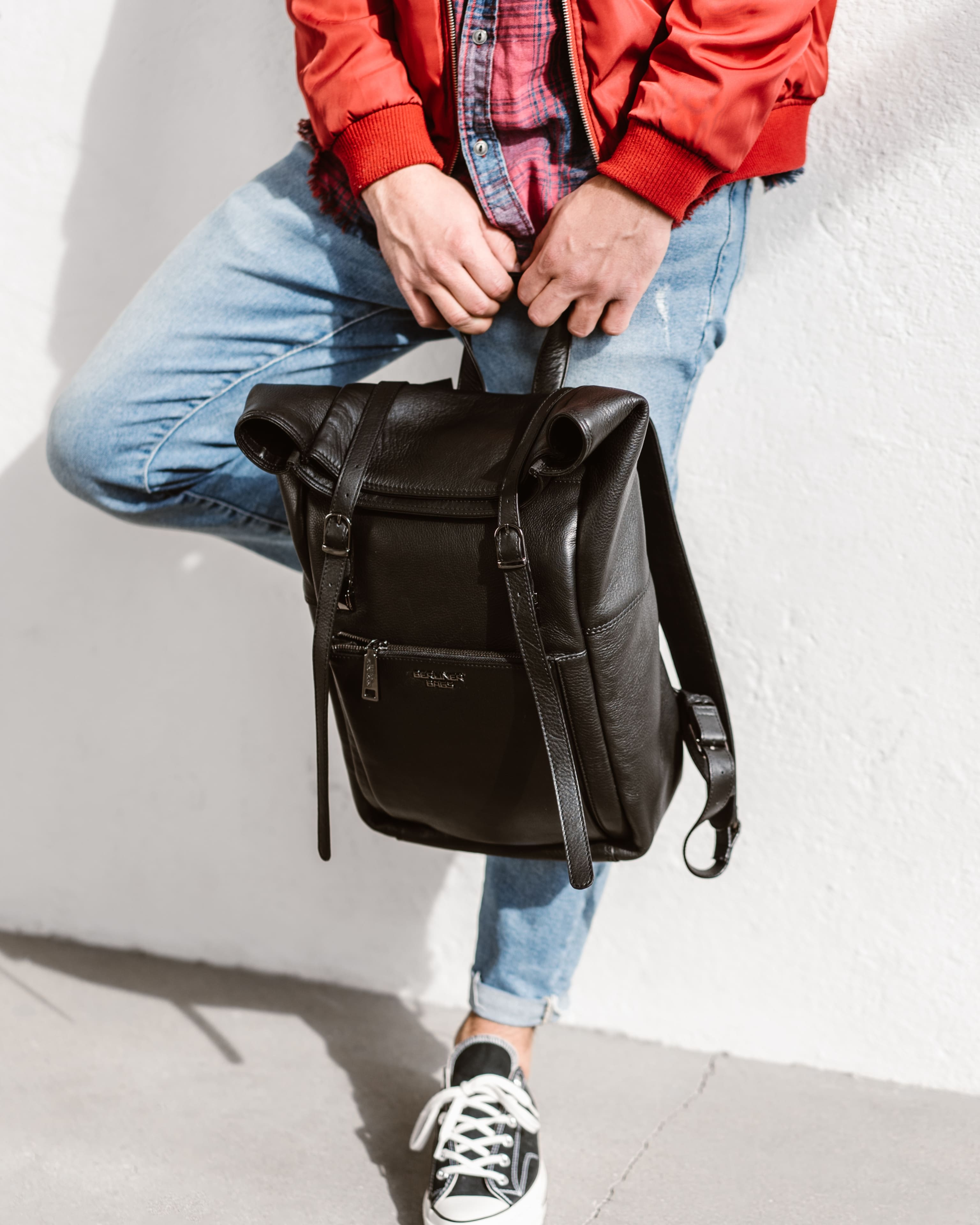 Side view of a person is carrying a black leather roll-top backpack