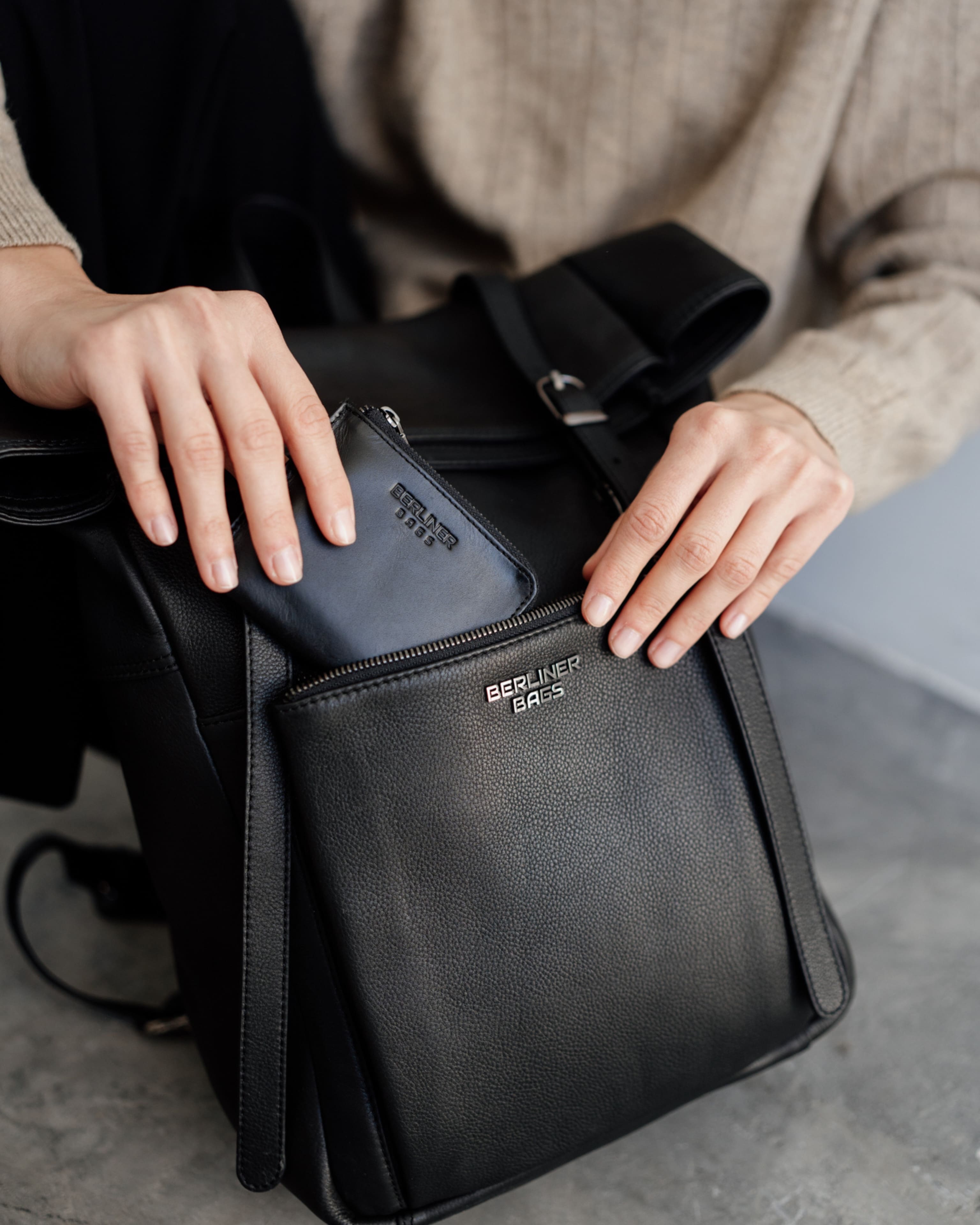 Close-up of hands sliding a wallet into the pocket of a black backpack