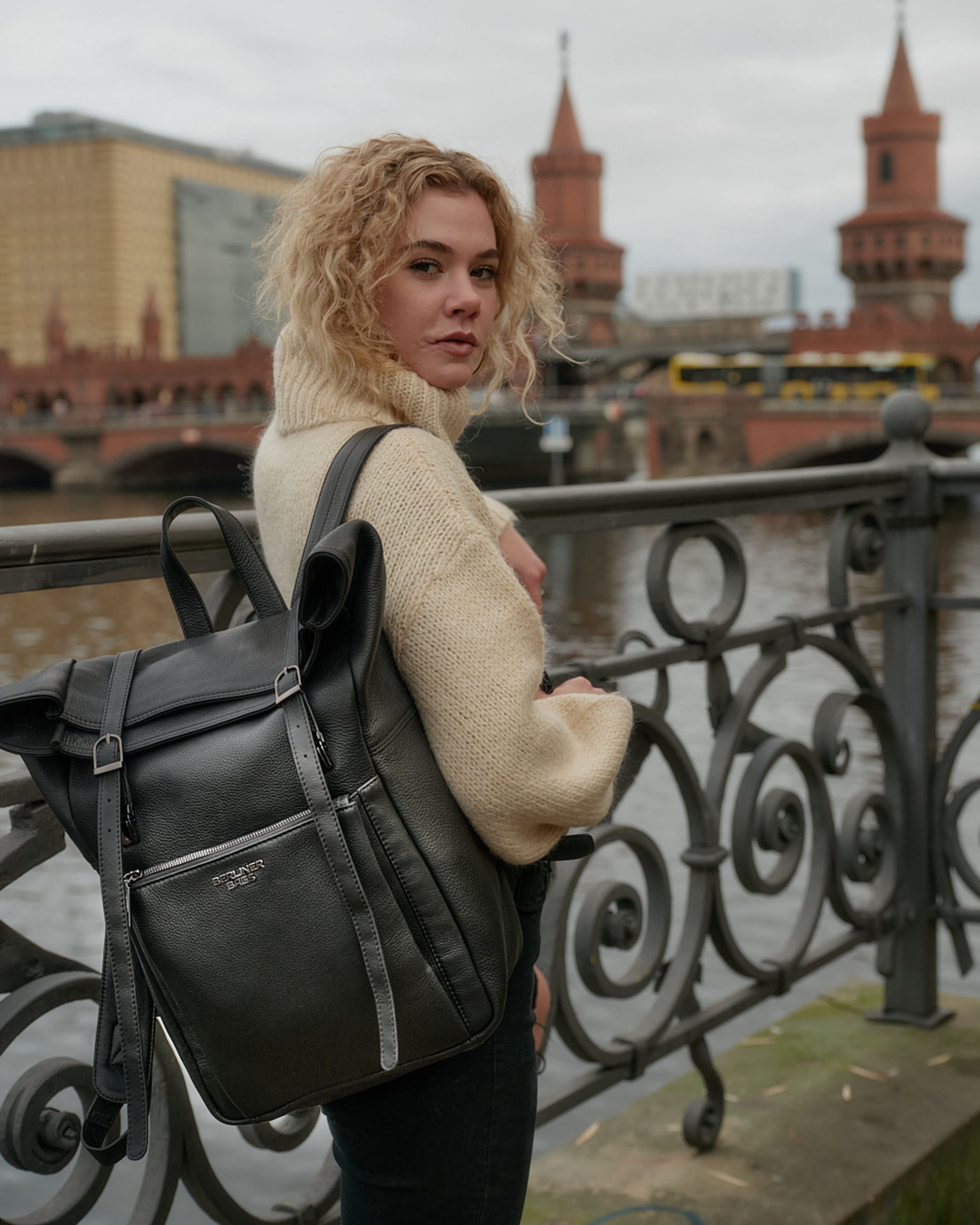 Over-the-shoulder view of a woman wearing a black leather roll-top backpack