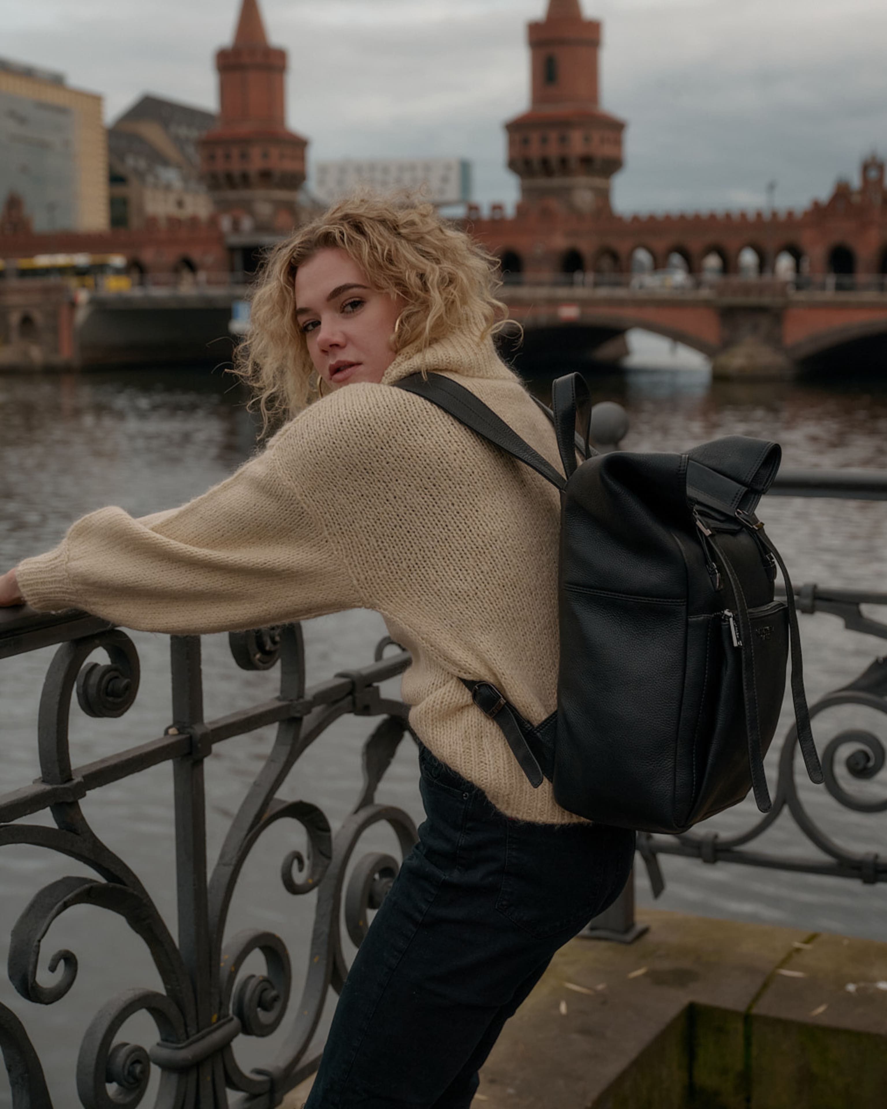 Woman leaning on a bridge railing while wearing a black roll-top backpack