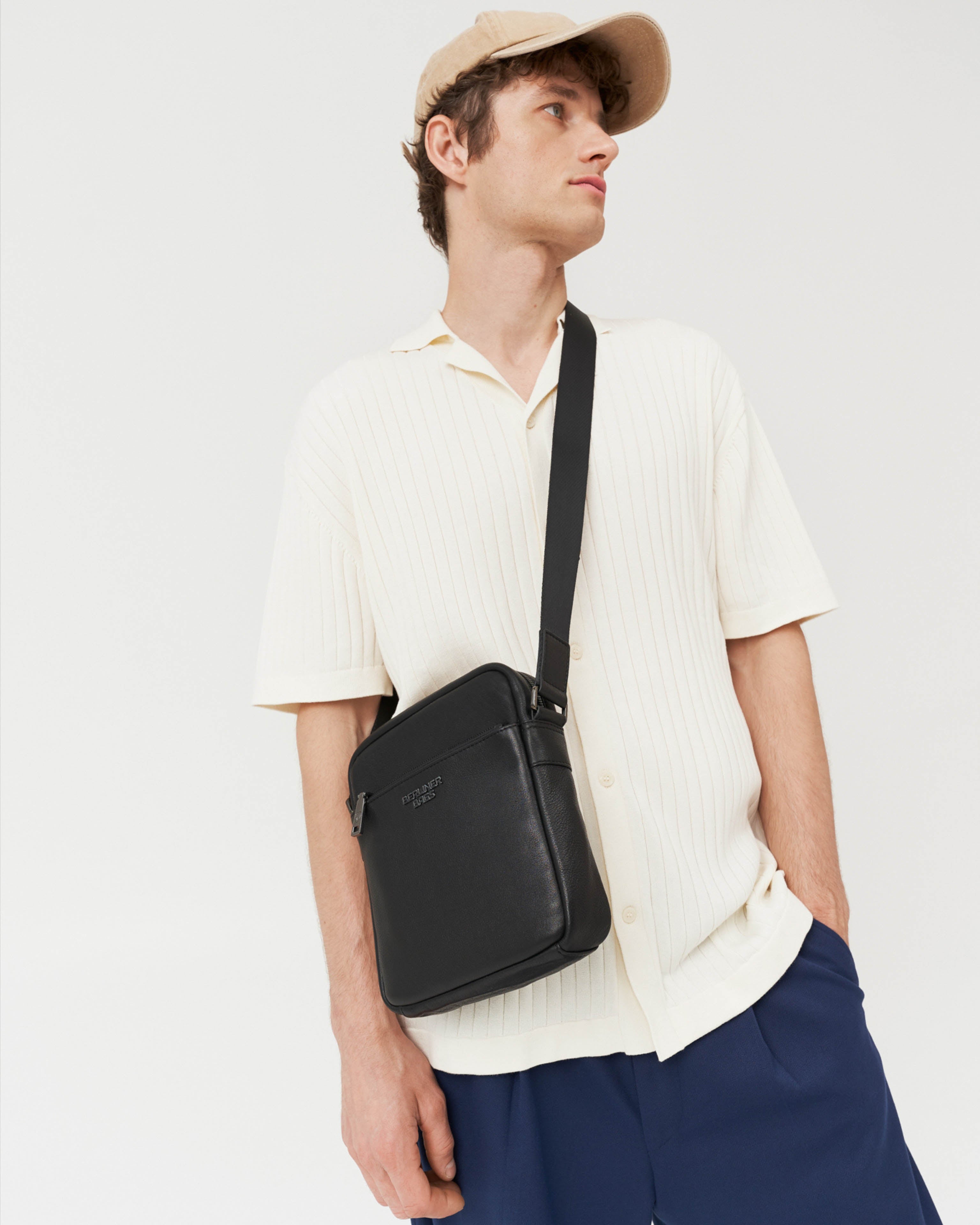 Angled front view of man wearing black leather crossbody messenger bag with strap