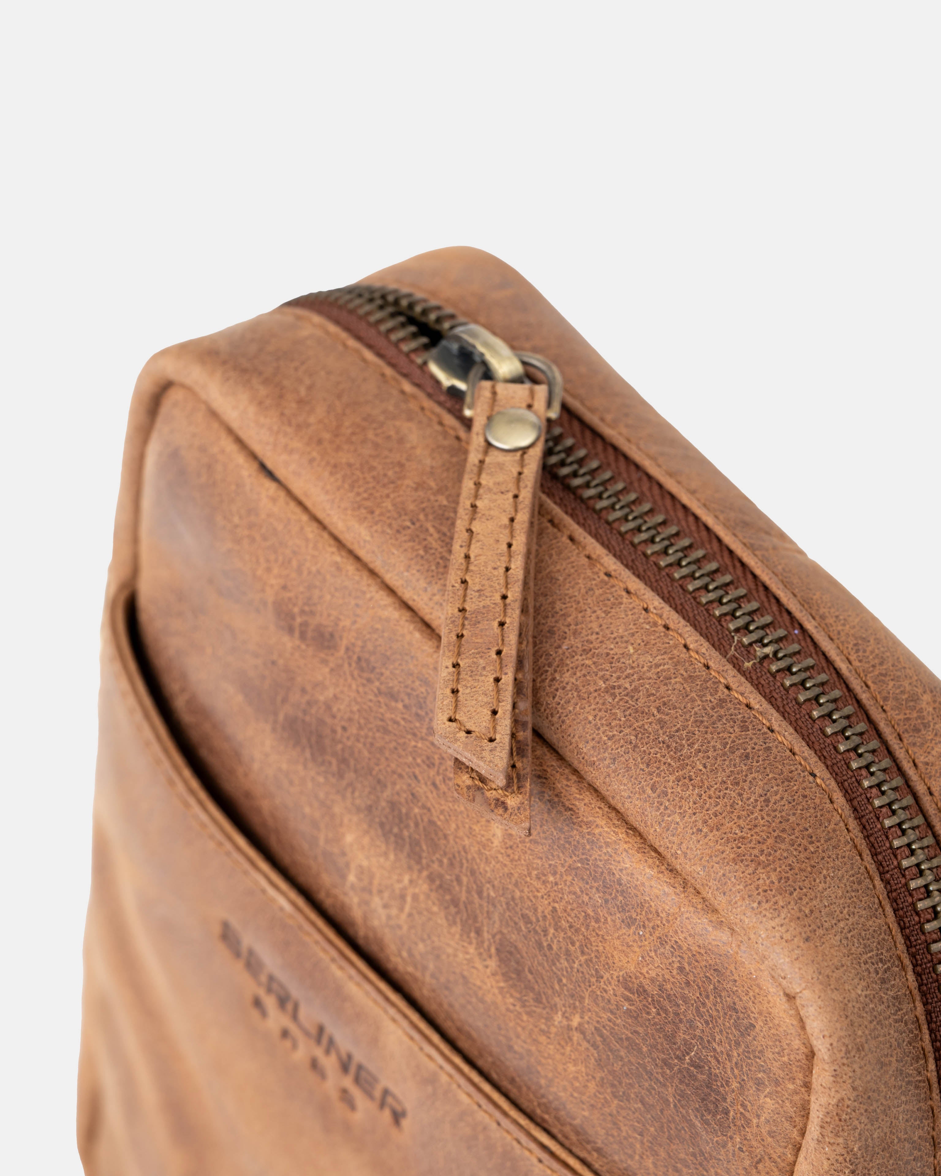 Close up view of the zipper hardware and leather pull on a camel leather messenger bag