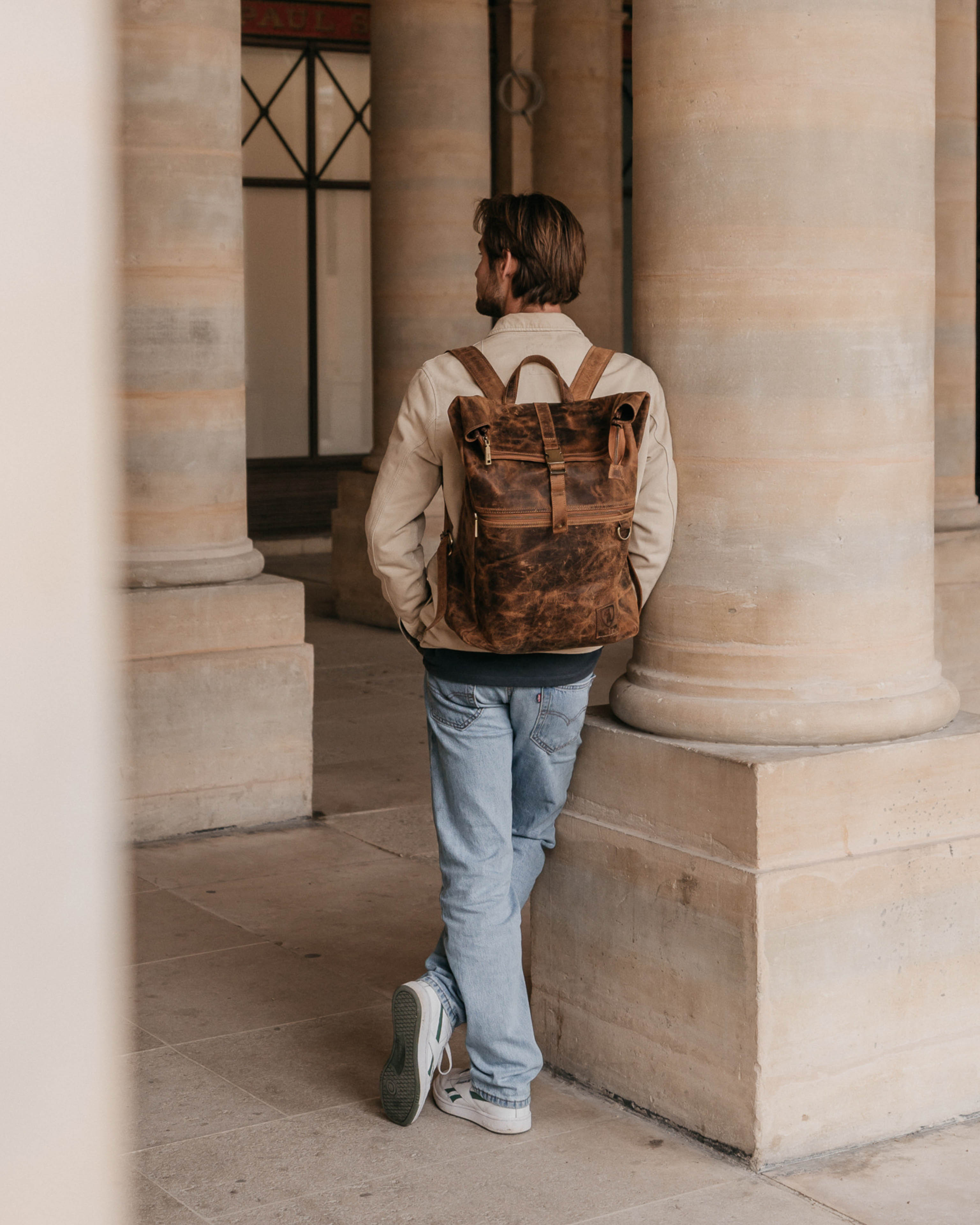 Man leaning against pillar wearing walnut leather backpack bag
