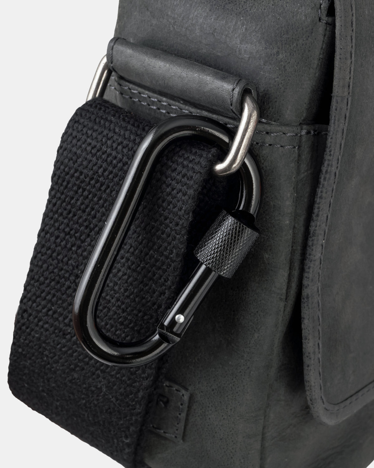 Close-up view of a black leather messenger bag showing a dark grey carabiner attached to the strap hardware