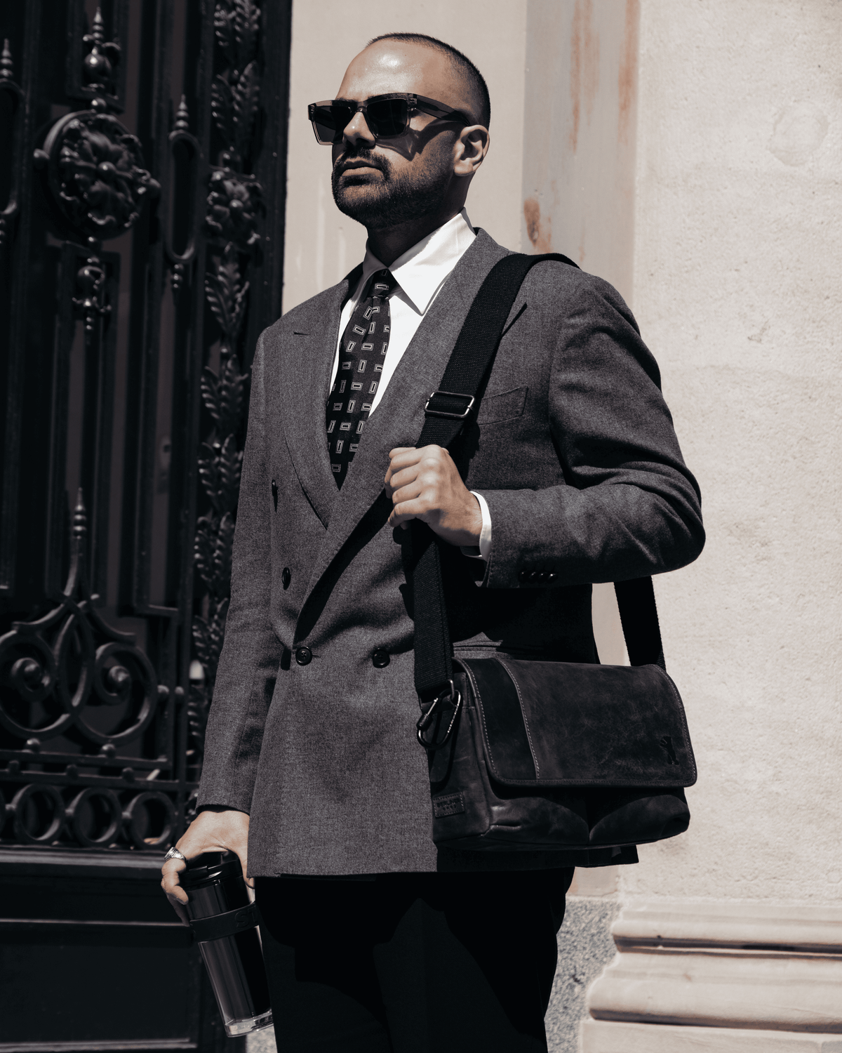 Three-quarter front view of a dark grey leather messenger bag worn on the shoulder by a man in a grey suit