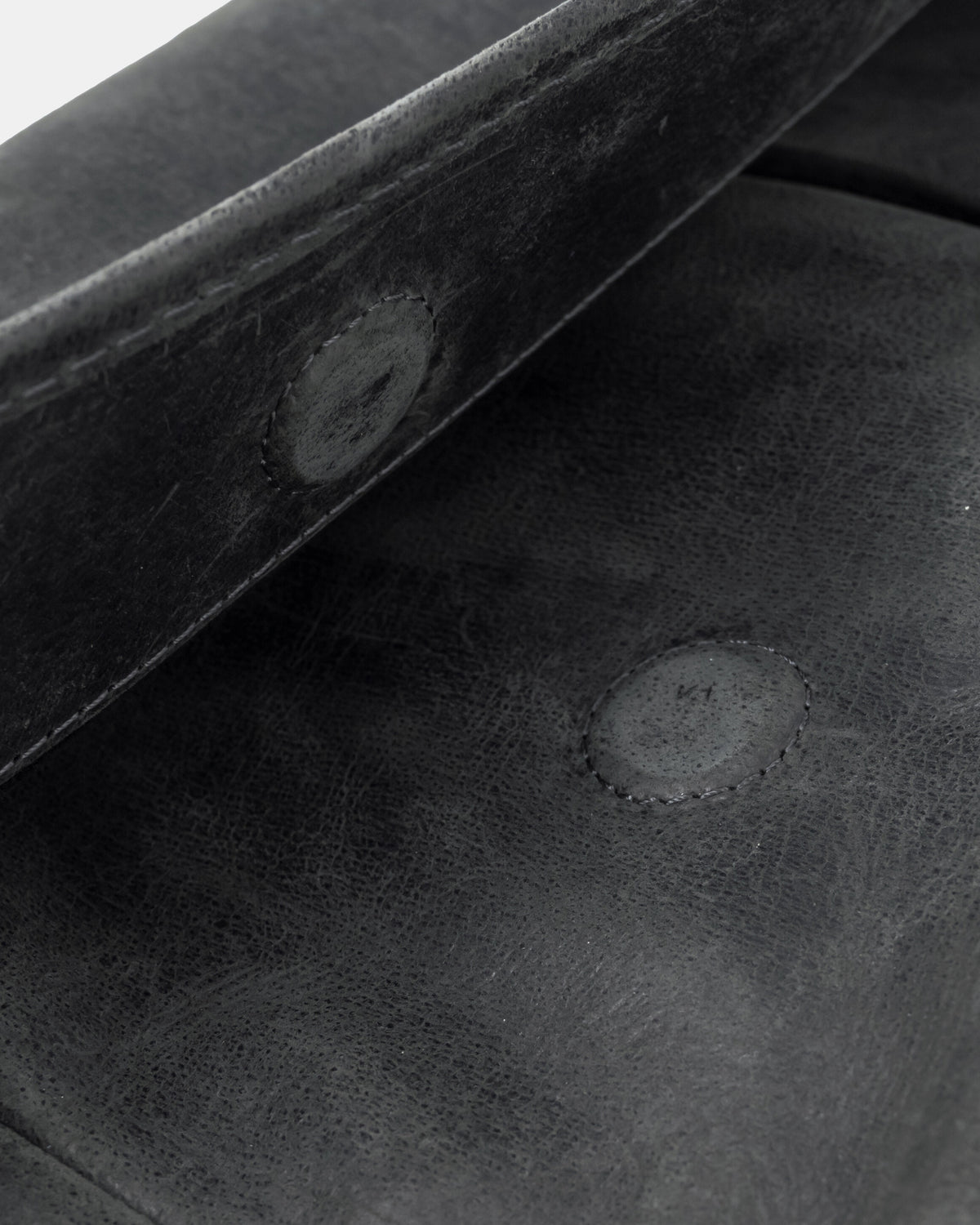 Close-up view of a dark grey leather messenger bag showing the magnetic snap closures hidden beneath the leather on the flap and front panel