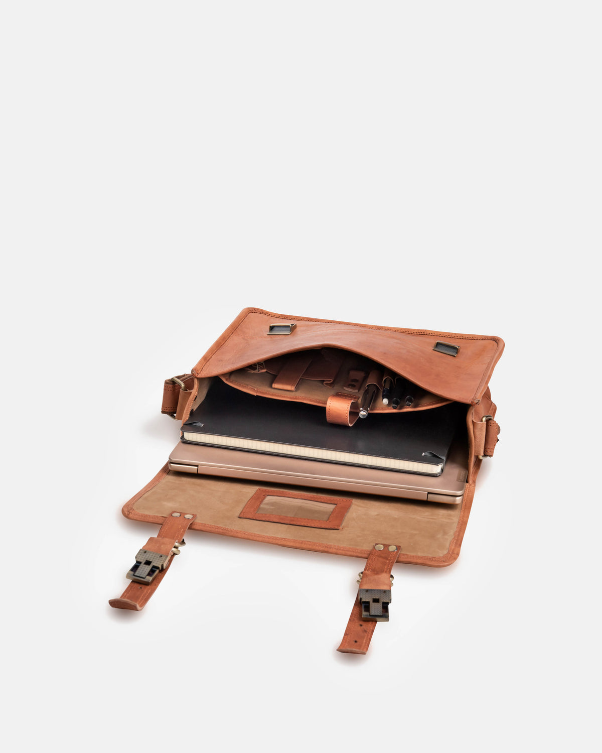 Top-down open view of a vintage leather briefcase or satchel messenger bag containing a laptop, a notebook, and pens in its organized internal compartments