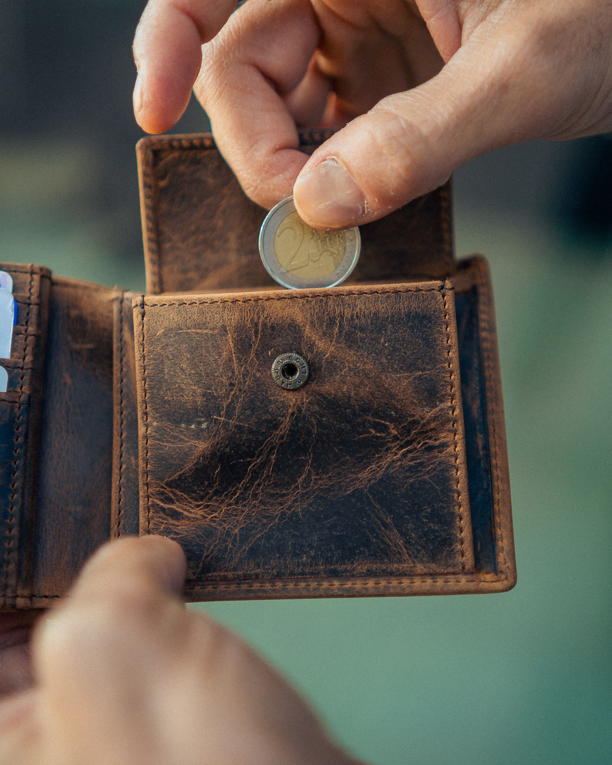 Man putting a coin in to a walnut leather wallet with ID flap