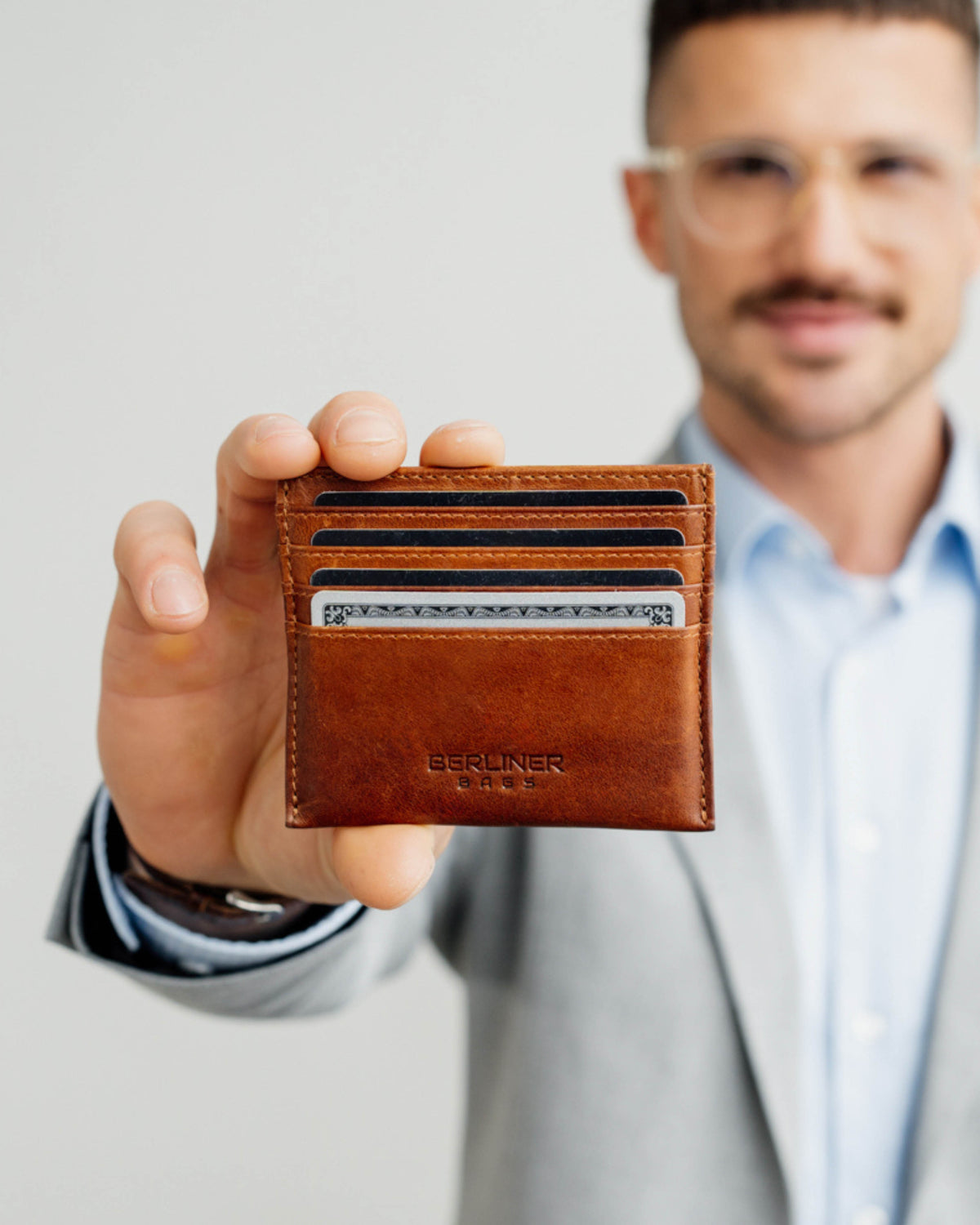 Man showing front view of cognac leather card case all slot filled with cards