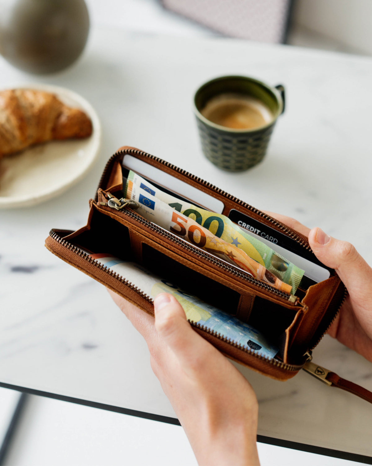 Hands opening suede cognac leather wallet with cash inside