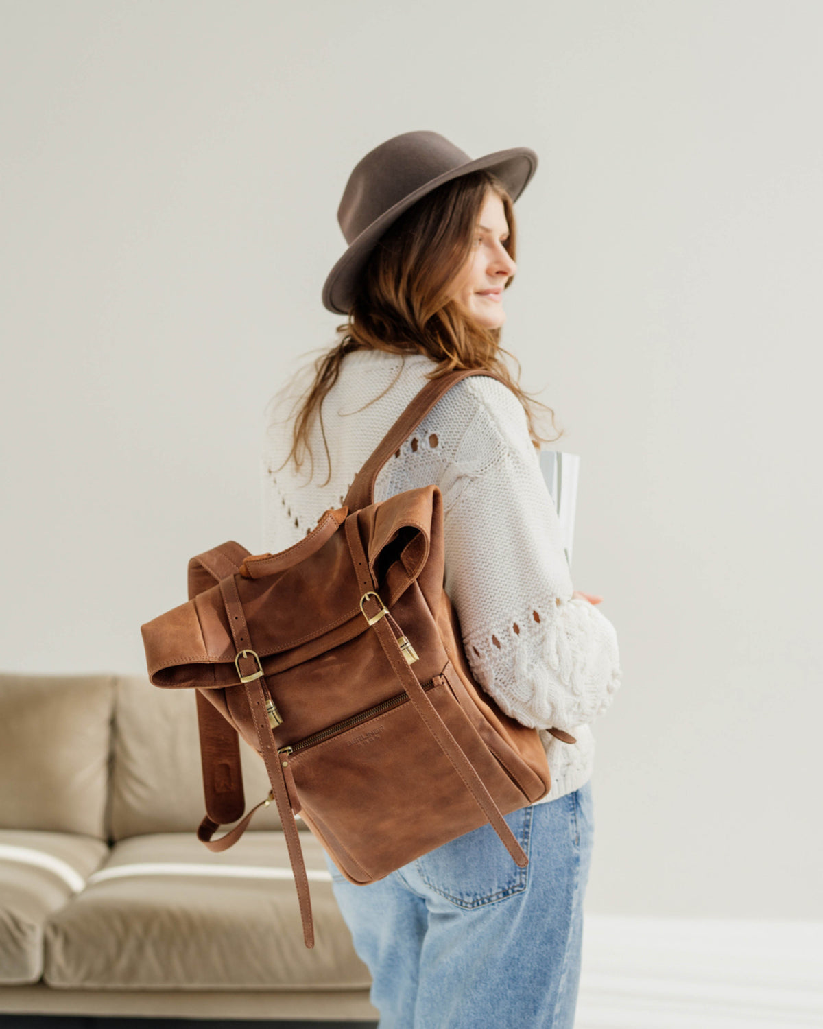 Rear view of a woman wearing a hat and carrying a camel roll-top backpack