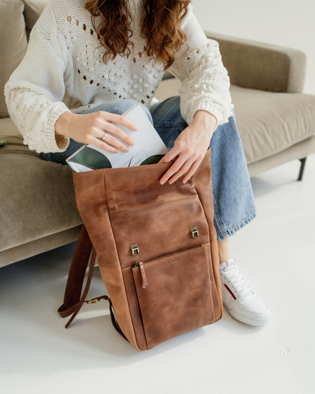 Shot of a woman sitting on a sofa sliding a magazine into a camel backpack