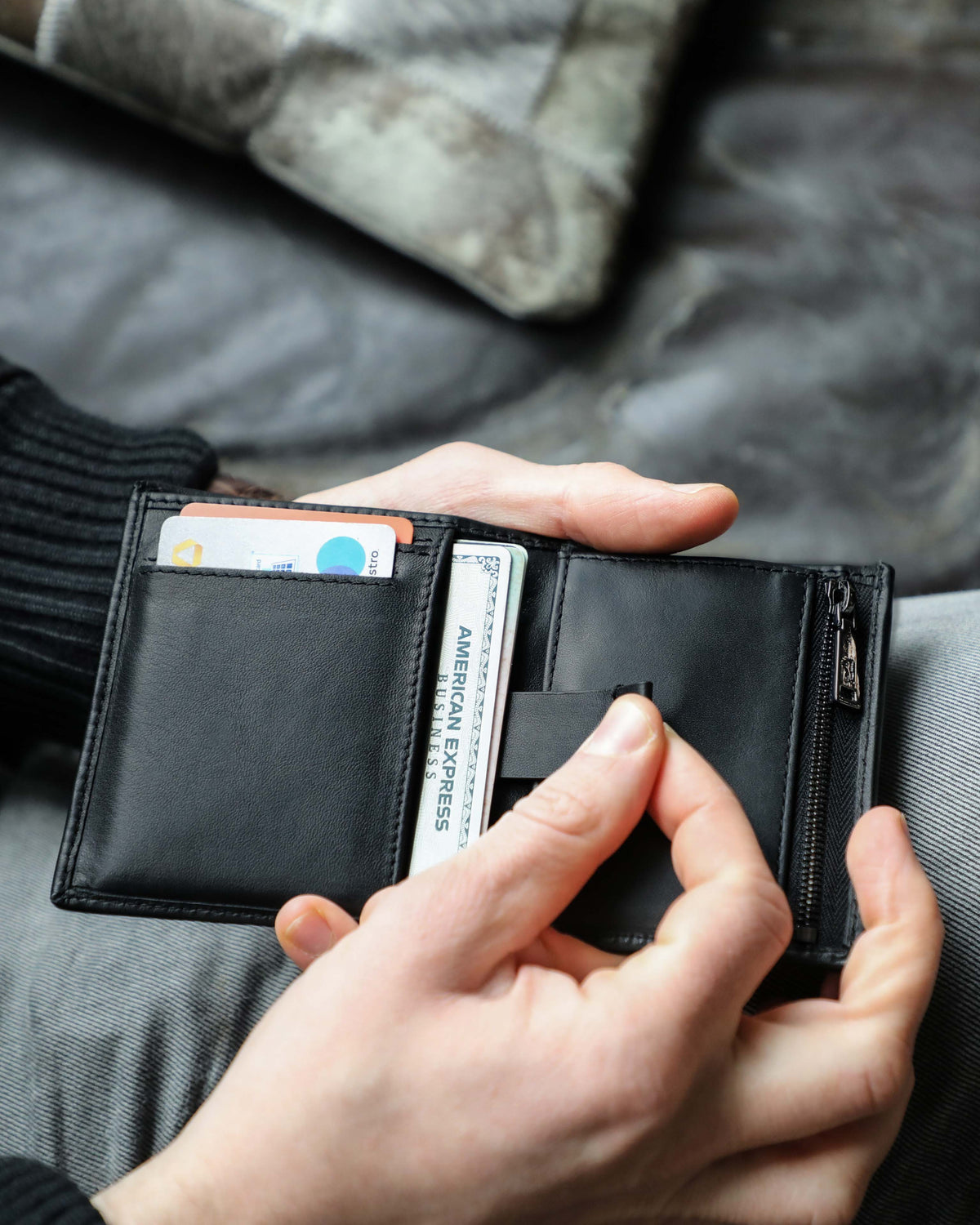 A person holding a emboss leather wallet with black zip featuring an interior card-pulling mechanism.
