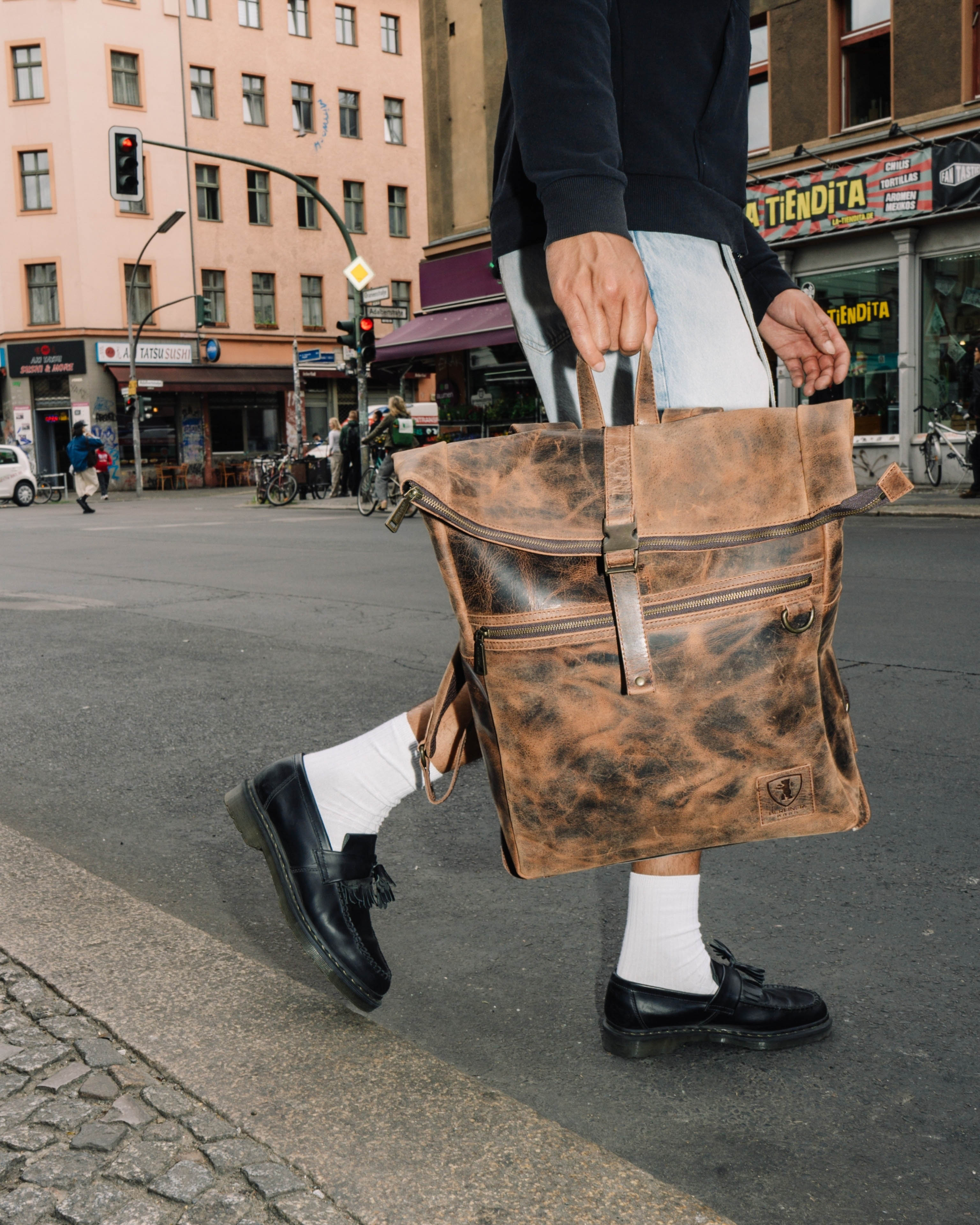 Man holding earth leather backpack while walking in the city