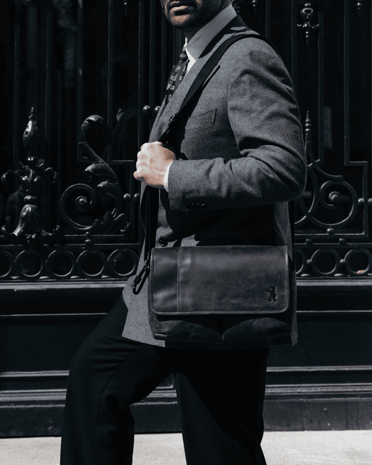 Side view of a dark grey leather messenger bag worn on the shoulder by a man in a suit