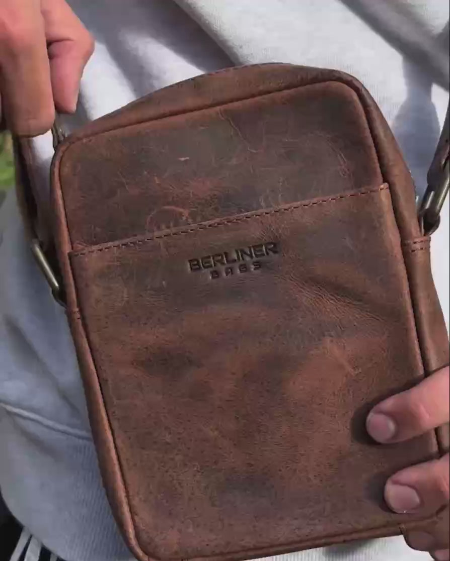 Close up of man holding a earth leather messenger bag with an embossed logo
